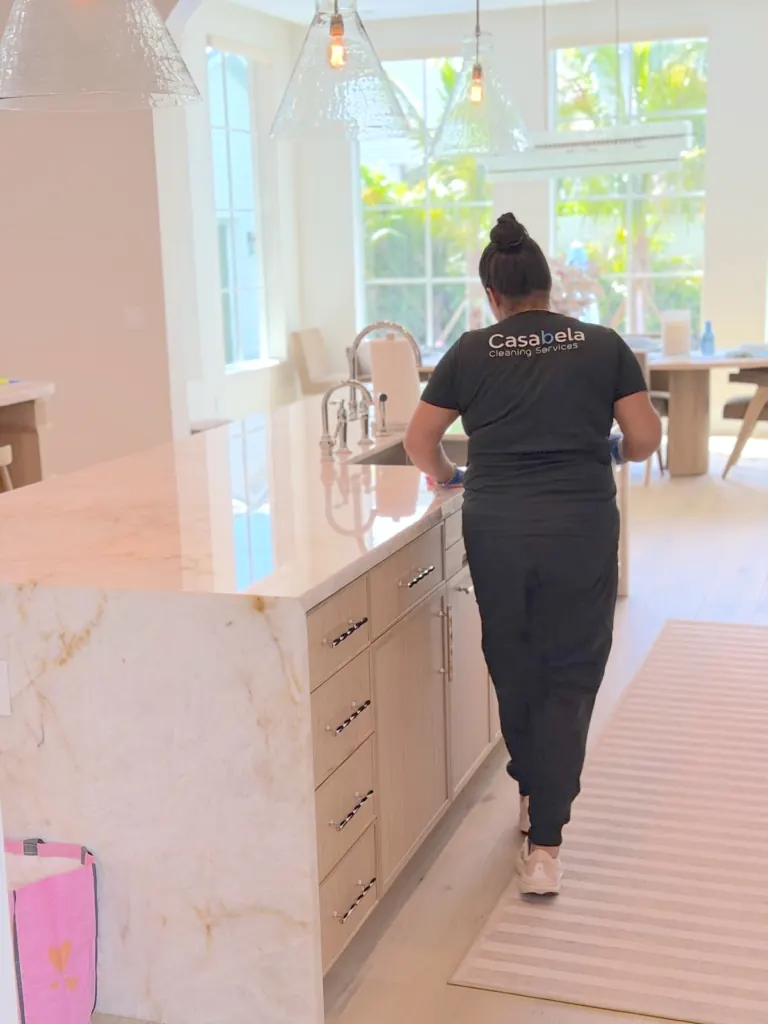 A Casabela cleaner in a black Casabela Cleaning Services tee wiping down a kitchen island in a bright South Florida home