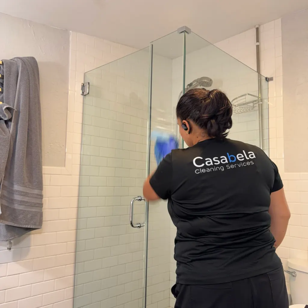 Casabela cleaner detailing a glass shower, the Casabela logo on the back of her shirt